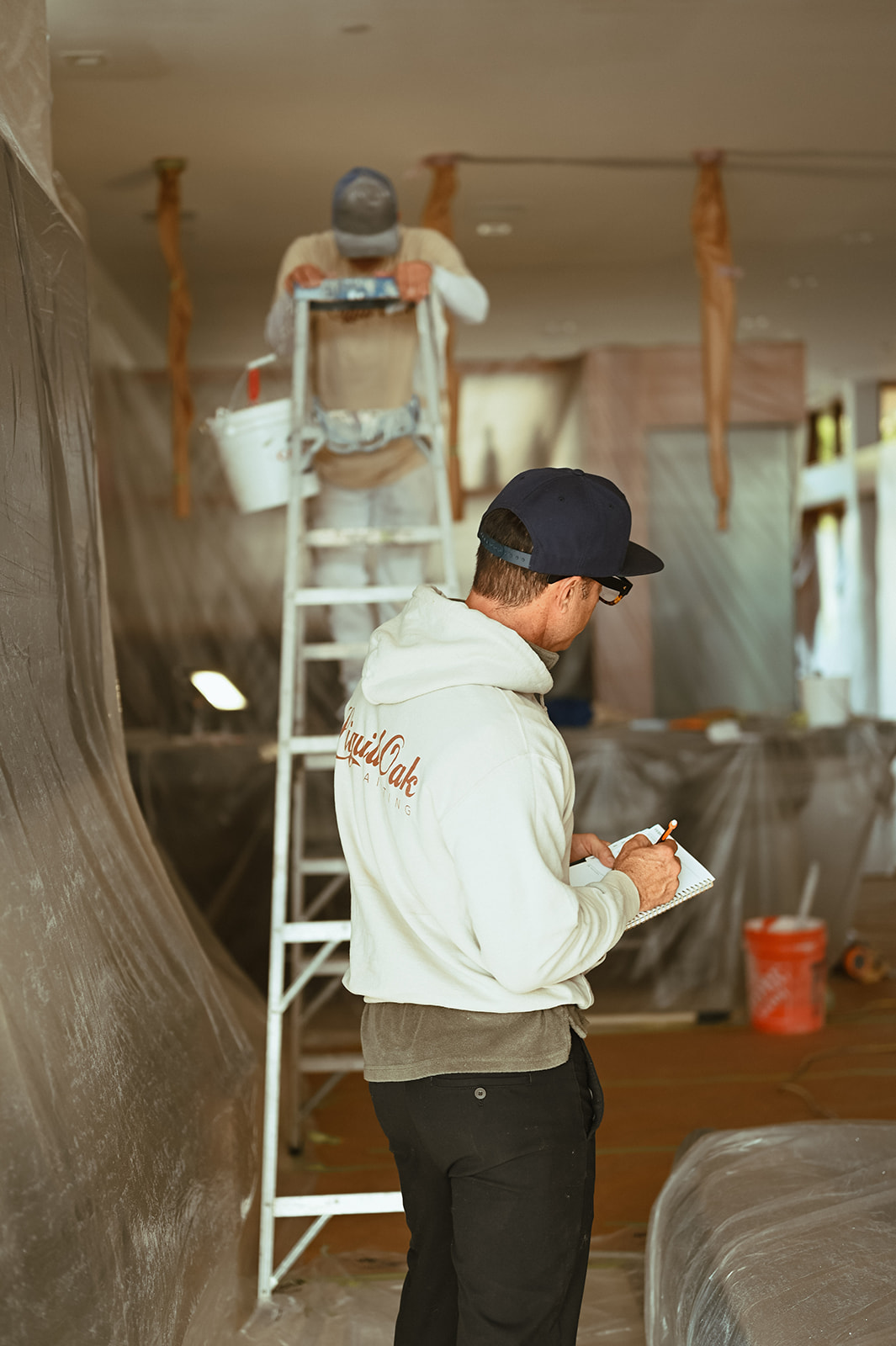 Interior painting work ongoing, painter on a ladder, furniture and fixtures tarped off for protection